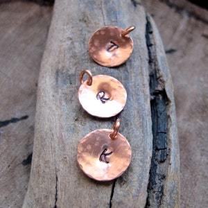 May include: Three copper disc charms with hammered textures and initial letters T, R, and K.
