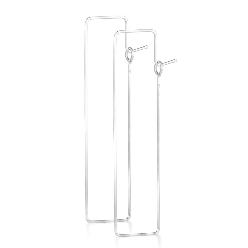 Puede incluir: Un par de pendientes de aro rectangulares de plata. Los pendientes son simples y de dise&ntilde;o moderno.