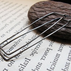 Puede incluir: Un par de pendientes de aro rectangulares negros. Los pendientes est&aacute;n hechos de metal fino y tienen un dise&ntilde;o simple y moderno.