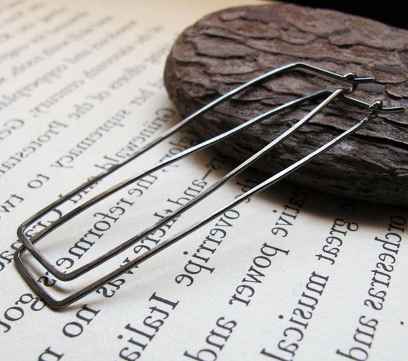 Puede incluir: Un par de pendientes de aro rectangulares negros. Los pendientes est&aacute;n hechos de metal fino y tienen un dise&ntilde;o simple y moderno.