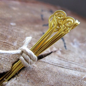 May include: A bundle of gold-colored wire headpins with a decorative spiral at the top. The headpins are tied together with a piece of twine.