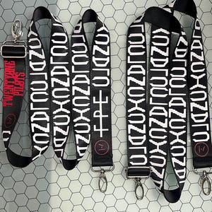 May include: Three black and white patterned straps with silver clasps. Each strap has a small black circle with a white number "1" inside. The strap on the left has the text "TWENTY ONE PILOTS" in red.