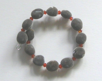 May include: A bracelet made of gray oval-shaped beads with small orange crystal beads in between.