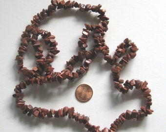 May include: A strand of brown and gold sunstone chip beads. The beads are irregular in shape and size. The strand is approximately 18 inches long.
