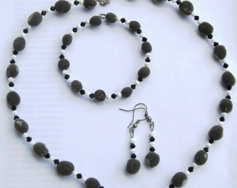 May include: A set of grey and black bead jewellery, including a necklace, bracelet, and earrings. The beads are oval-shaped and have a mottled appearance.
