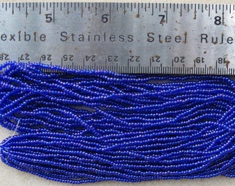 May include: A close-up of a large quantity of small, round, blue glass beads. The beads are arranged in rows and are measured against a ruler that reads "Flexible Stainless Steel Ruler".