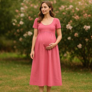 May include: A dusty rose maternity dress with a scoop neckline and short sleeves. The dress features a fitted bodice and a flowing skirt, designed for comfort and style during pregnancy. The model is standing in a garden setting.