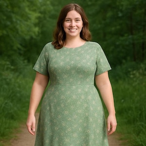 Puede incluir: Un vestido verde claro con un estampado floral. El vestido tiene mangas cortas y una cintura ajustada. La persona de la imagen sonríe y está de pie en un camino en una zona boscosa.