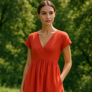 Op de afbeelding: Een vrouw draagt een feloranje, korte mouwen, wikkeljurk met een V-hals.