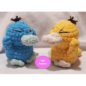 May include: Two handmade crochet plush toys, one blue and one yellow, resembling cartoon characters. Each has a white bill and feet, with a small brown tuft of hair. The toys are sitting side by side.
