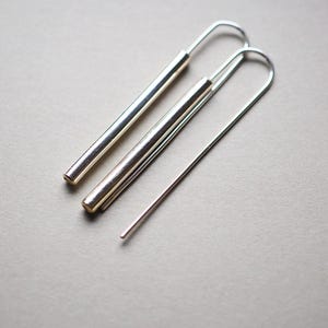 Puede incluir: Un par de pendientes de aro de plata con un dise&ntilde;o largo, delgado y recto. Los pendientes est&aacute;n hechos de metal y tienen un estilo simple y minimalista.
