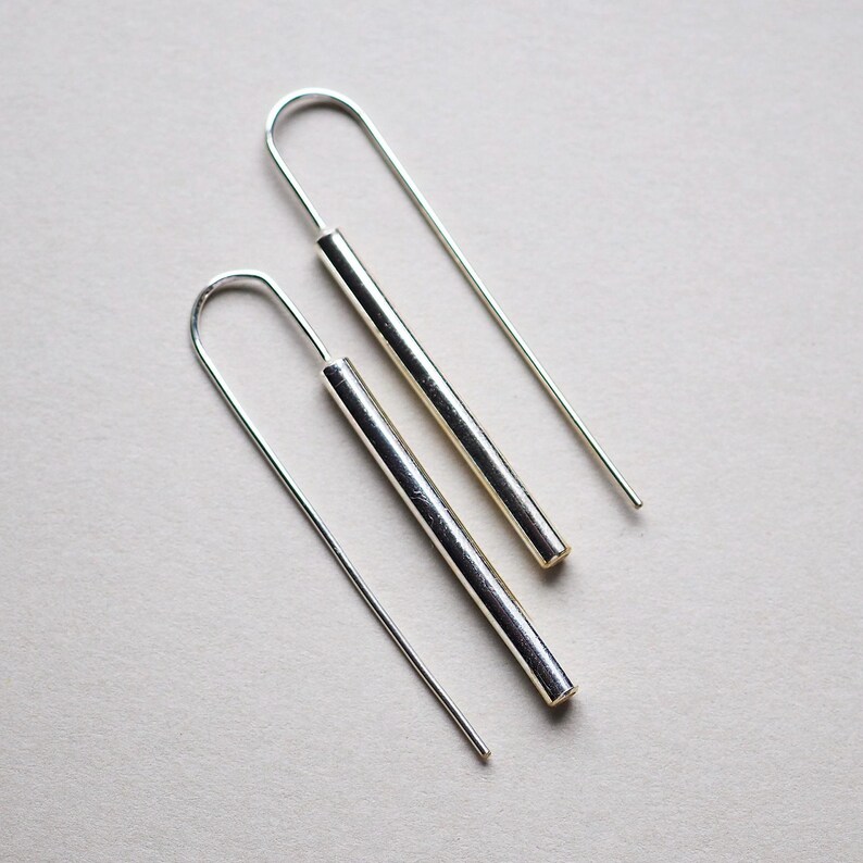 Puede incluir: Un par de pendientes de aro de plata con alambres largos, delgados y rectos y un colgante de barra de plata en cada alambre.
