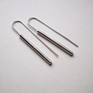 Puede incluir: Un par de pendientes de aro de plata con alambres largos, delgados y rectos y una barra cil&iacute;ndrica m&aacute;s gruesa que cuelga de cada alambre.