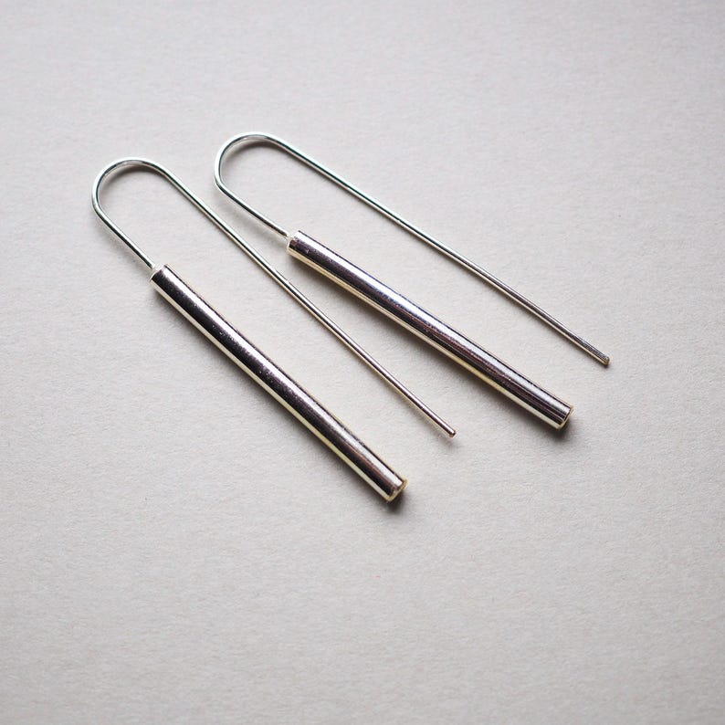 Puede incluir: Un par de pendientes de aro de plata con alambres largos, delgados y rectos y una barra cil&iacute;ndrica m&aacute;s gruesa que cuelga de cada alambre.