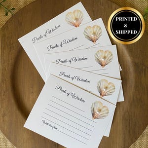 May include: A stack of white cards with the text "Pearls of Wisdom" in elegant script, each featuring a watercolor seashell design with a pearl. The cards are arranged on a wooden plate, with a "PRINTED & SHIPPED" sticker.