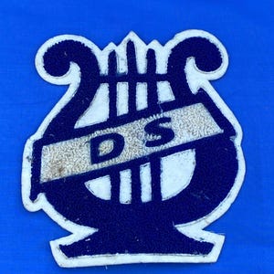 May include: A blue and white felt patch with a lyre design and the letters "D.S." in the center.