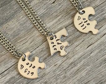 May include: Three silver necklaces with puzzle piece pendants. The pendants say "Big Sis", "Lil Sis", and "My Lil Sis".