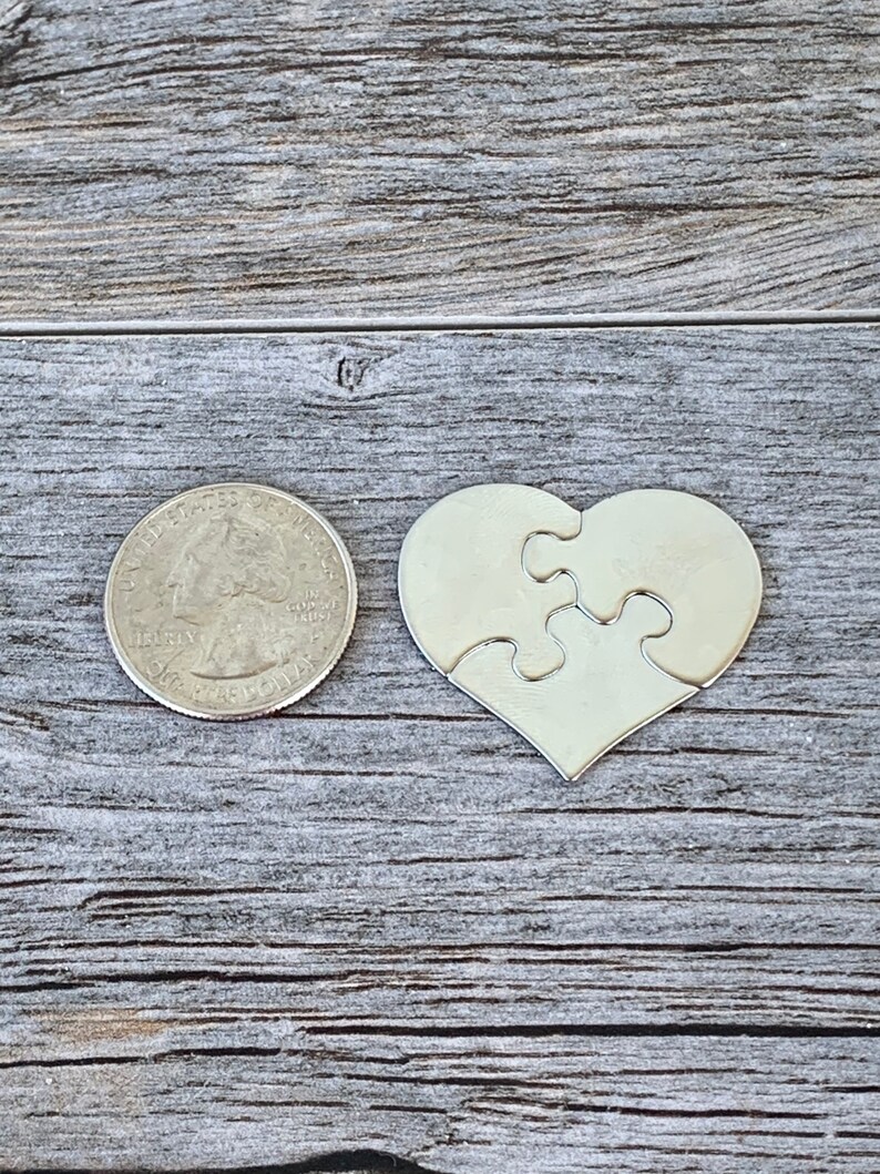 May include: A silver metal heart-shaped puzzle piece with four interlocking pieces. The puzzle piece is about the size of a US quarter.