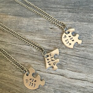 May include: Three silver necklaces with puzzle piece pendants. The pendants have the words "Best Sis", "Wild Sis", and "Lil Sis" engraved on them.