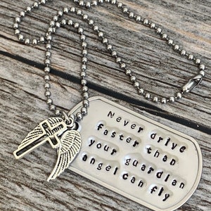 May include: A silver necklace with a dog tag pendant that reads "Never drive faster than your guardian angel can fly". The pendant has a small cross and angel wings charm attached.