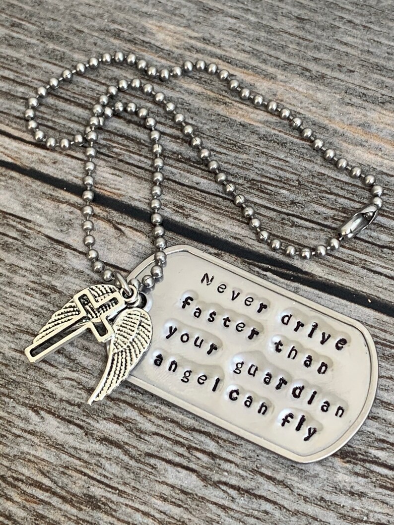 May include: A silver necklace with a dog tag pendant that reads "Never drive faster than your guardian angel can fly". The pendant has a small cross and angel wings charm attached.