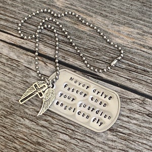 May include: Silver necklace with a silver dog tag pendant that reads "Never drive faster than your guardian angel can fly". The dog tag has a silver cross with wings attached to it.