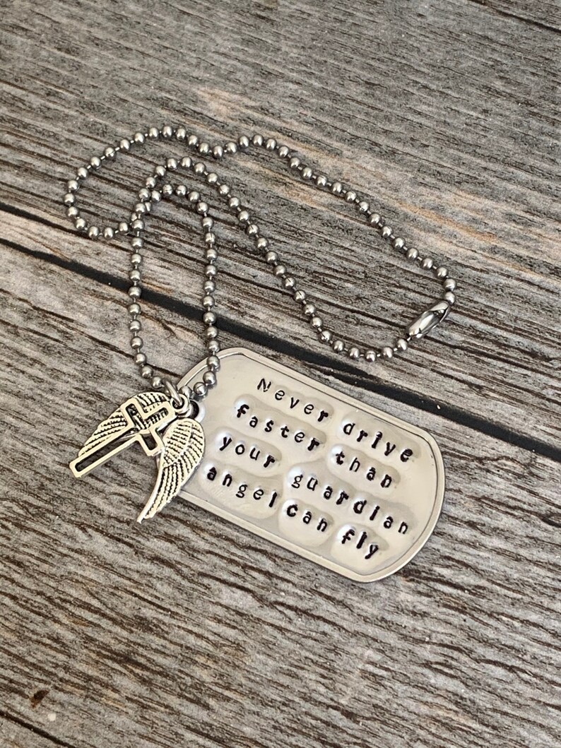 May include: Silver necklace with a silver dog tag pendant that reads "Never drive faster than your guardian angel can fly". The dog tag has a silver cross with wings attached to it.