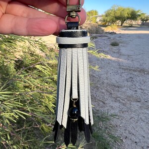 May include: Black and white leather tassel keychain with a black bead and a gold metal clasp.