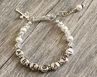 May include: A silver charm bracelet with white beads and a silver cross charm. The bracelet spells out the name "Abigail".