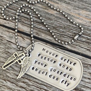 May include: Silver necklace with a dog tag pendant that reads "Never drive faster than your guardian angel can fly". The pendant has a small silver cross and angel wings attached to it.