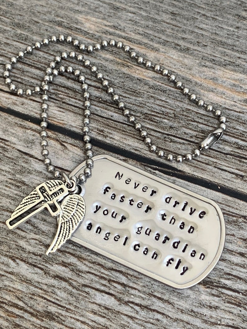 May include: Silver necklace with a dog tag pendant that reads "Never drive faster than your guardian angel can fly". The pendant has a small silver cross and angel wings attached to it.