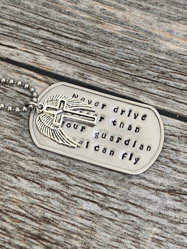 May include: Silver dog tag necklace with a cross and wings charm. The tag reads "Never drive faster than your guardian angel can fly."