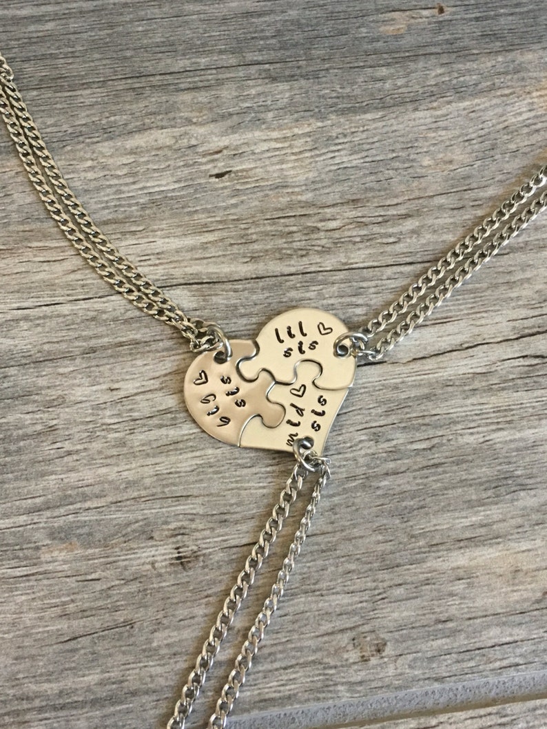 May include: Three silver necklaces with heart-shaped puzzle pieces that say "lil sis" and "big sis".