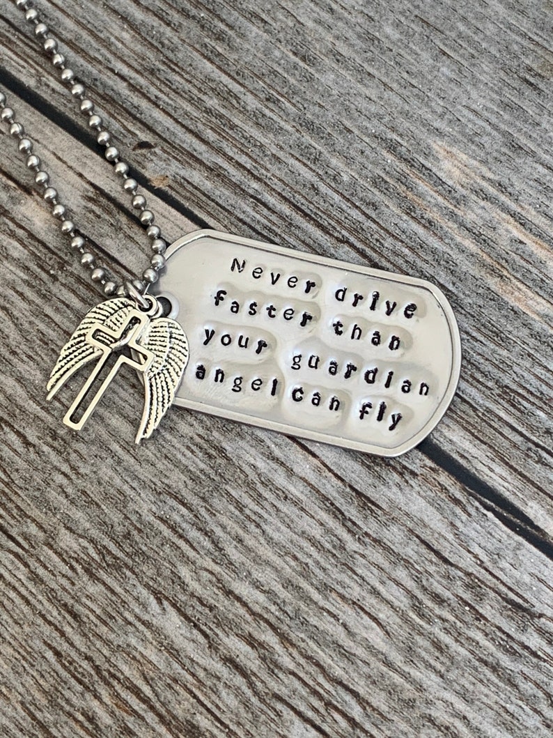 May include: Silver necklace with a dog tag pendant that reads "Never drive faster than your guardian angel can fly". The dog tag is attached to a silver chain with a small angel wing charm.