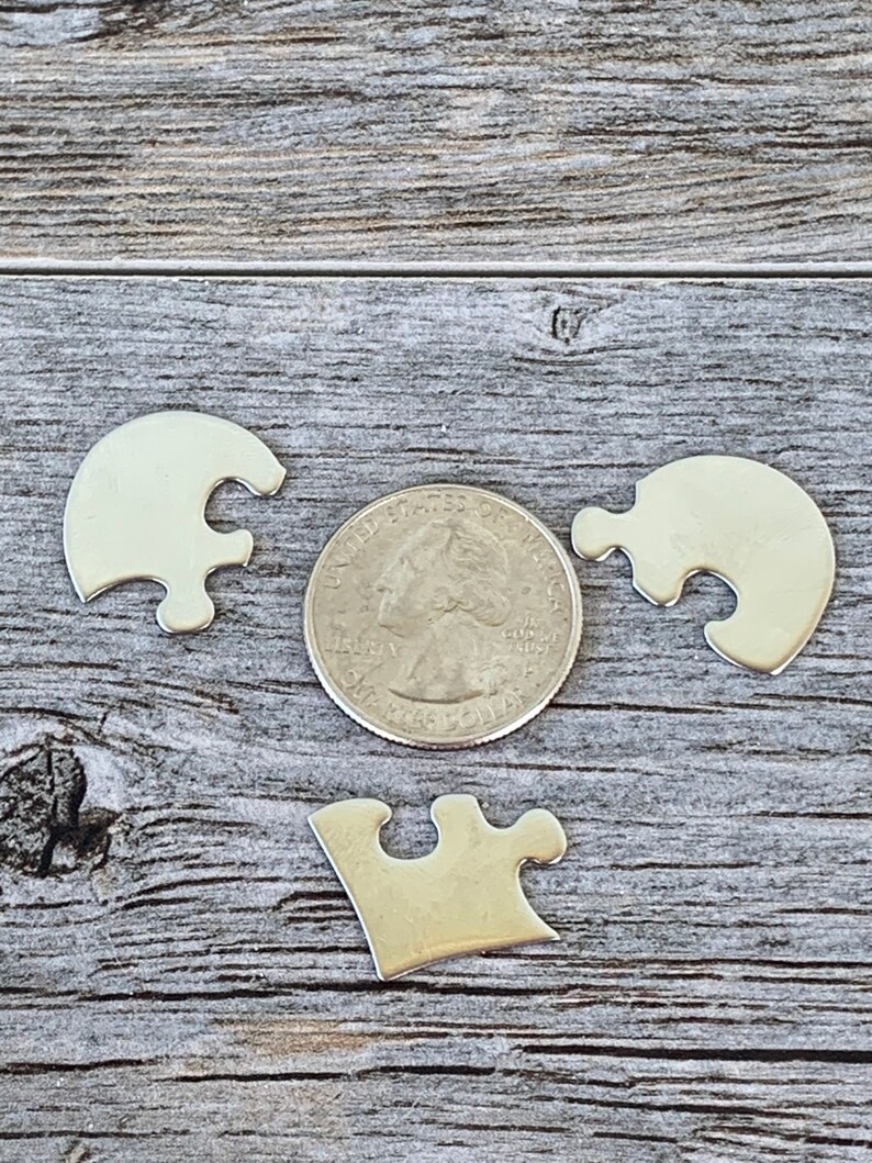 May include: Three silver puzzle pieces in the shape of a puzzle piece. The pieces are about the size of a quarter.