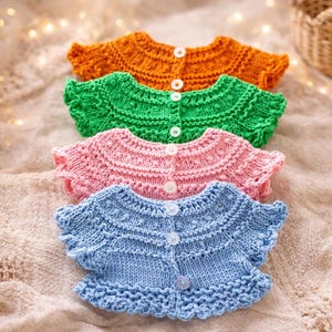 May include: Four colorful knitted baby cardigans in orange, green, pink, and blue. Each cardigan has a round neckline, short sleeves, and is fastened with white buttons. The cardigans are arranged in a row, showcasing their vibrant colors and intricate knit details.