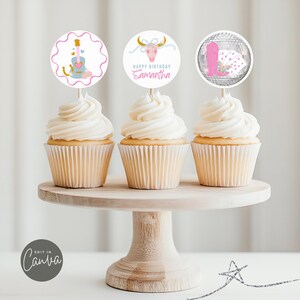 以下が含まれることがあります： 白いフロスティングをかけたカップケーキが3つ、丸い紙製のカップケーキトッパーで飾られています。トッパーには、ピンクのギター、金色の角のある頭蓋骨、ピンクのブーツが付いたディスコボールが描かれています。頭蓋骨のトッパーには「Happy Birthday Samantha」という文字が書かれています。