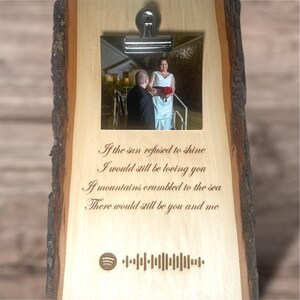 May include: A wooden plaque with a photo of a couple in front of a building. The plaque has a quote engraved on it that reads: "If the sun refused to shine I would still be loving you If mountains crumbled to the sea There would still be you and me". There is a Spotify logo and a barcode below the quote.