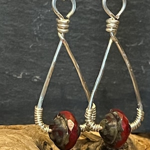 May include: Silver dangle earrings with a red and black swirl glass bead on each earring.