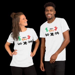May include: Two people wearing white t-shirts with the words "Tuck & Roll" and a graphic of a skateboarder in green, red, and black. The shirts are short-sleeved and the people are smiling.