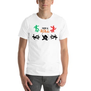 May include: White t-shirt with the words "TUCK & ROLL" in orange and green text. The shirt features stick figure illustrations demonstrating the tuck and roll technique. The illustrations are in green, red, and black.