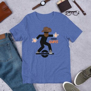 May include: Blue t-shirt with a graphic of a cartoon figure wearing a cowboy hat and sunglasses, with the words "FINGER GUNS" in orange. The figure is riding a black one-wheel board.