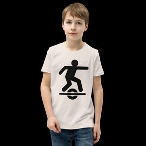 May include: A light beige t-shirt featuring a black graphic of a person riding a one-wheel electric unicycle. The graphic shows a stick figure balancing on a wheel. The shirt is worn by a young person.