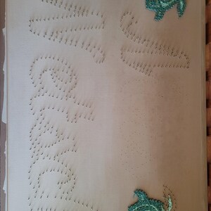 May include: A beige background with two green turtle silhouettes made of tacks. The word "Seashells" is spelled out in tacks on the left side of the image. The word "Seashells" is spelled out in tacks on the right side of the image.