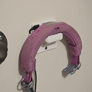 May include: A pink pet collar with a charging dock attached to a wall outlet. The collar has a silver buckle and a white charging port.