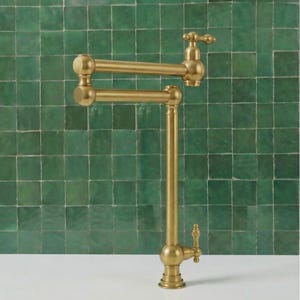 May include: A gold-coloured, articulated pot filler tap with a classic design. The tap features a double-jointed arm for extended reach and a decorative handle. The background is a green tiled wall.