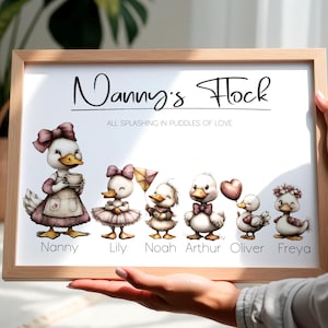 Puede incluir: Impresión enmarcada con un borde de madera clara. La ilustración en acuarela muestra patos, con el texto "Nanny's Flock" arriba y "All Splashing in Puddles of Love" abajo. Cada pato está vestido y nombrado de forma única.