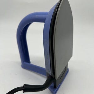 Puede incluir: Una plancha eléctrica gris y negra con un asa y una base azules. La plancha tiene una punta y un cable de alimentación negro. El asa es curva y la base es de color azul claro.