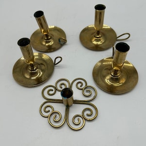 Könnte beinhalten: Eine Sammlung von Vintage-Kerzenhaltern aus Messing. Das Set enthält vier einzelne Kerzenhalter mit kreisförmigen Basen und einen dekorativen, durchbrochenen Kerzenhalter mit einem Wirbeldesign. Die Kerzenhalter sind in verschiedenen Größen und Formen.