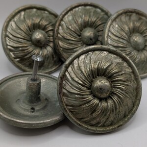 May include: Five antique-style cabinet knobs with a distressed silver finish. Each knob features a circular design with a central, raised sphere and radiating, textured lines. One knob has a screw attached.